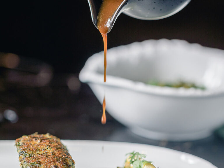 Gourmetgericht mit feiner Sauce angerichtet auf dunklem Teller im Sternerestaurant Maerz und Maerz