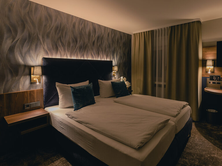Stimmungsvoll abgedunkeltes Hotelzimmer im Hotel Rose mit großem, einladendem Bett